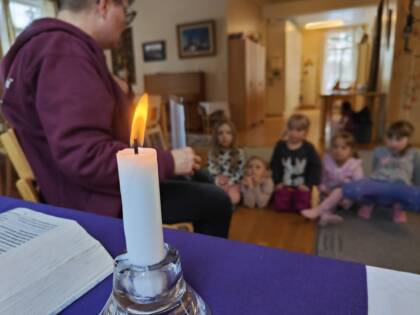Kuva kerhosta, jossa lapset istuvat lattialla ja kynttilä palaa pöydällä.
